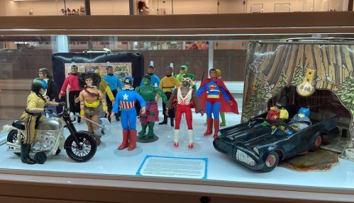 A display case featuring various action figures, including superheroes and characters, alongside a vintage toy vehicle.
