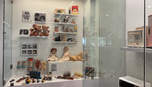 Display case featuring vintage toys, dolls, and photographs, showcasing nostalgic childhood items.