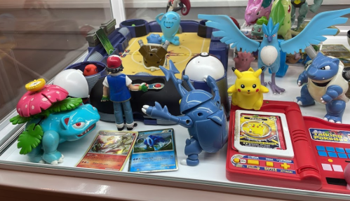 A display of Pokémon toys, including figures of Pikachu, Blastoise, and Venusaur, along with trading cards and a game board.