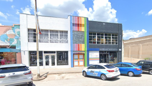 Colorful storefronts line a street, featuring a mix of modern and vintage architecture under a bright blue sky.