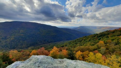 A panoramic view of colorful autumn foliage covering rolling hills under a partly cloudy sky.