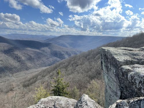 A panoramic view of a mountainous landscape with rocky cliffs and rolling hills under a partly cloudy sky.