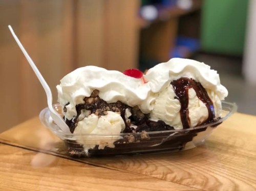 A delicious ice cream sundae with two scoops, chocolate sauce, whipped cream, nuts, and a cherry on top, served in a dish.