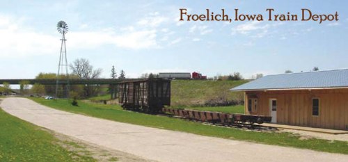 Froelich, Iowa train depot with a wooden building, train cars, and a windmill in a grassy landscape under a blue sky.