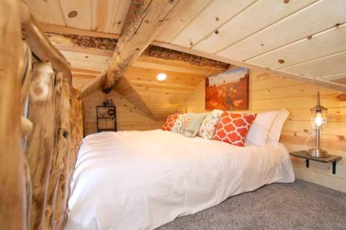Cozy loft bedroom with a wooden ceiling, a double bed, decorative pillows, and a rustic lantern.