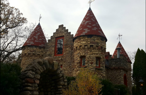 A whimsical stone castle with red-tiled roofs and turrets, surrounded by trees and autumn foliage.