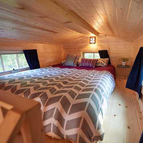 Cozy loft bedroom with a large bed, wooden walls, and natural light from windows, decorated with pillows and curtains.