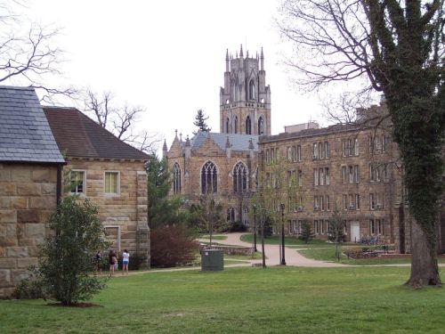 A scenic view of a college campus featuring a stone building and a tall, ornate tower in the background.