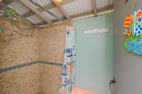 A bright outdoor shower with a colorful curtain, stone walls, and decorative signs, creating a relaxing atmosphere.