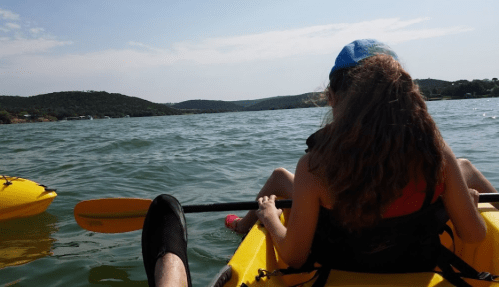 A person kayaking on a lake, with a view of hills in the background and another kayak nearby.