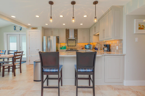 Modern kitchen with light gray cabinets, granite countertops, and two bar stools. Bright lighting and stainless steel appliances.