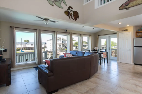 Bright living area with large windows, a brown sofa, dining table, and coastal decor overlooking a waterfront view.