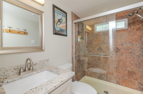 A modern bathroom featuring a glass shower, granite countertop, and decorative mirror.