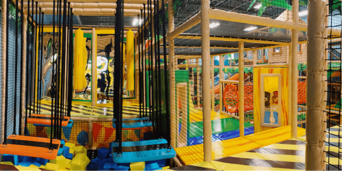 A colorful indoor playground with climbing structures, nets, and soft play areas for children.