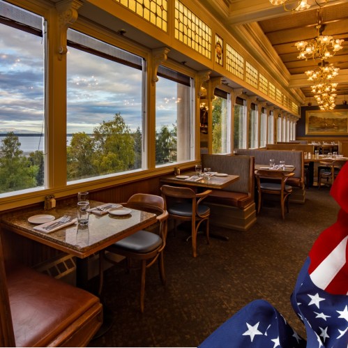 Cozy restaurant interior with large windows, scenic views, and elegant decor, featuring tables set for dining.