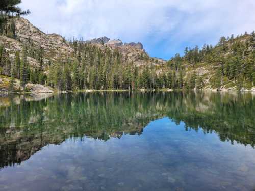 A serene lake reflecting mountains and trees under a blue sky, surrounded by lush greenery.