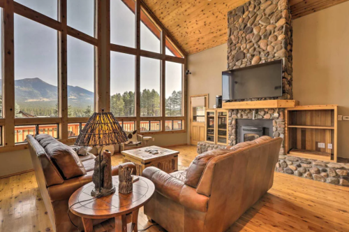 Cozy living room with large windows, stone fireplace, wooden accents, and mountain views.