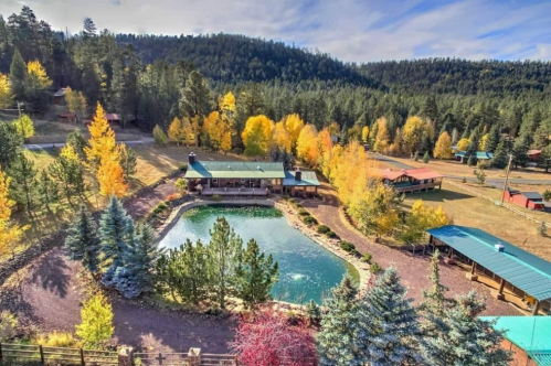 A scenic view of a lodge by a pond, surrounded by colorful autumn trees and rolling hills.