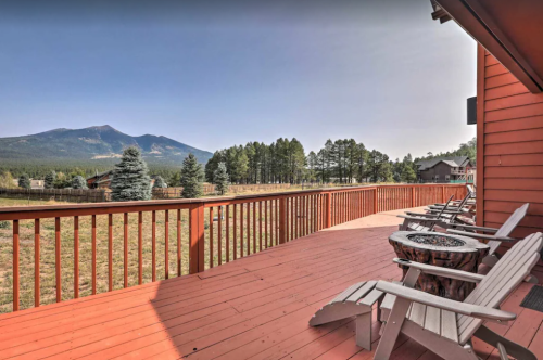 A wooden deck with chairs overlooks a scenic landscape of mountains and trees under a clear sky.