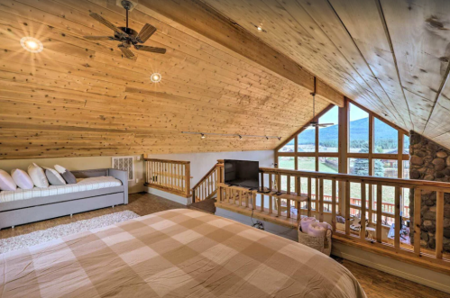 Cozy loft bedroom with wooden ceiling, large windows, and a comfortable bed overlooking a scenic view.