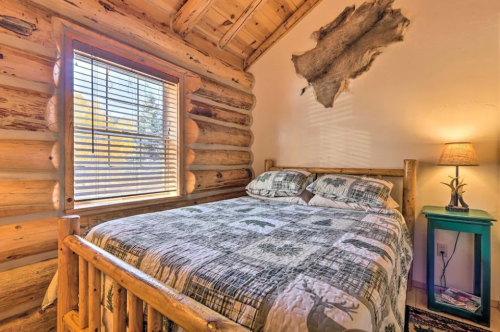 Cozy log cabin bedroom with a wooden bed, patterned bedding, and a window letting in natural light.