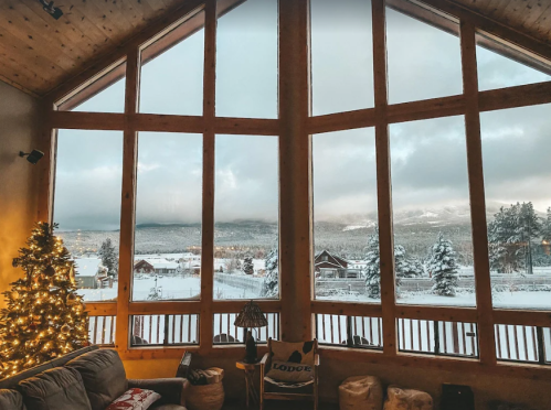 Cozy living room with a Christmas tree, large windows showcasing a snowy mountain landscape outside.