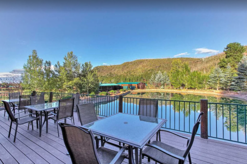 A scenic view from a deck overlooking a calm pond surrounded by trees and mountains under a clear blue sky.