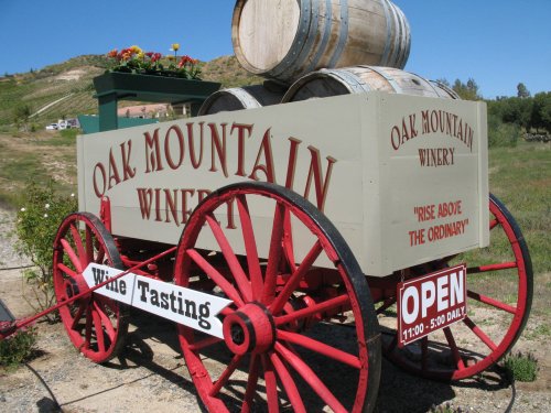 A vintage wagon with barrels, advertising Oak Mountain Winery and wine tasting, set against a vineyard backdrop.