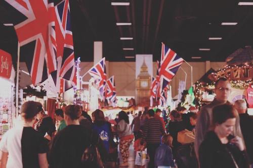 A bustling market scene with British flags, people shopping, and festive decorations in a lively atmosphere.