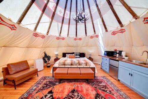 Cozy interior of a glamping tent featuring a bed, seating area, kitchenette, and decorative rug.