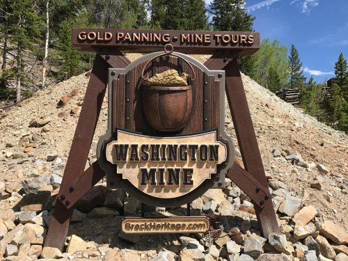 Sign for Washington Mine offering gold panning and mine tours, set against a backdrop of trees and rocky terrain.