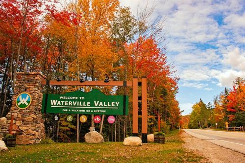 A welcome sign for Waterville Valley surrounded by vibrant autumn foliage and a clear blue sky.