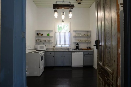 A bright kitchen with gray cabinets, a white stove, and modern appliances, viewed through an open door.