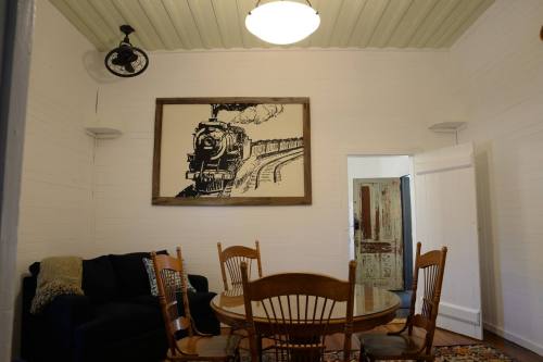 Cozy room with a train-themed artwork, a round dining table, wooden chairs, and a dark sofa.