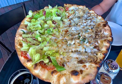 A large pizza divided in half, one side topped with lettuce and tomatoes, the other with cheese and chicken.