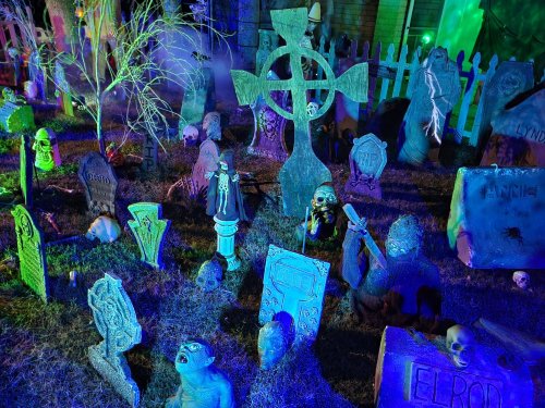 A spooky graveyard scene with glowing tombstones, eerie statues, and a cross, all illuminated in blue and green light.