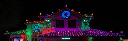 A house decorated with colorful lights and pumpkins for Halloween, featuring a spooky theme and vibrant colors.