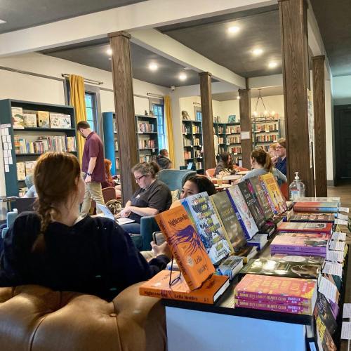 A cozy bookstore with people reading and working, surrounded by shelves of books and colorful displays.