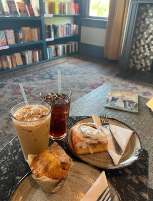 A cozy café scene with iced coffee, iced tea, a muffin, and a cinnamon roll on a table, surrounded by bookshelves.
