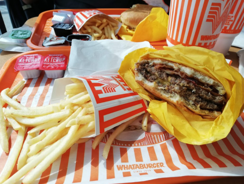 A tray with a Whataburger, fries, ketchup packets, and a drink, all on an orange and white striped tray.