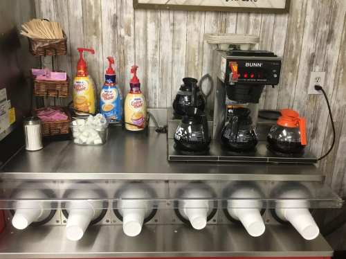 Coffee station with creamers, sugar, and a BUNN coffee maker, featuring multiple coffee pots and dispensers.
