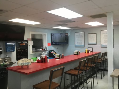 A cozy diner interior with a red counter, bar stools, a TV, and menu specials on the wall.