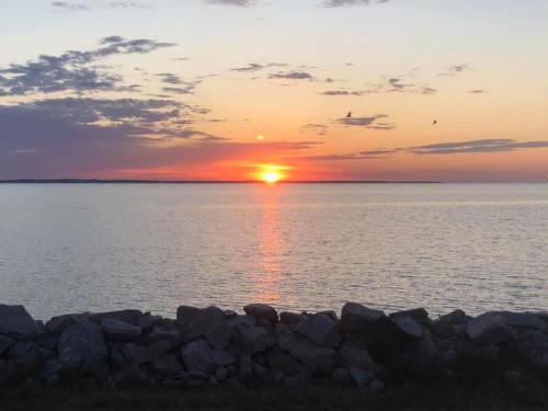 A serene sunset over calm waters, with colorful clouds and a rocky shoreline in the foreground.