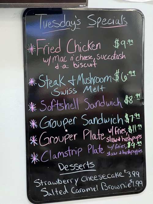 Menu board listing Tuesday's specials: Fried Chicken, Steak & Mushroom Melt, Softshell Sandwich, Grouper Plate, Clamstrip Plate, Desserts.