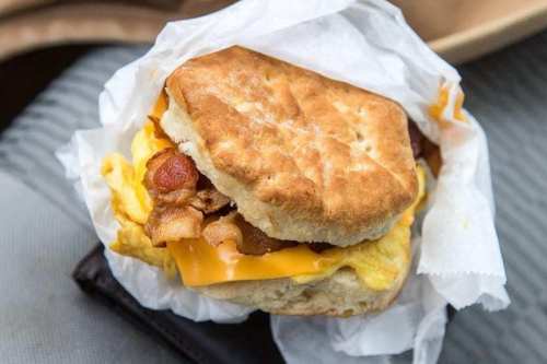 A biscuit sandwich filled with bacon, cheese, and scrambled eggs, wrapped in paper.