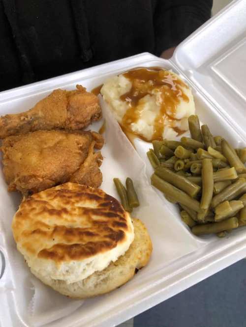 A takeout container with fried chicken, mashed potatoes with gravy, green beans, and a biscuit.