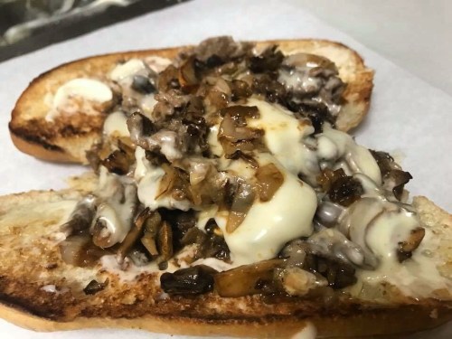 A toasted sandwich filled with sautéed mushrooms, onions, and melted cheese on a white paper background.