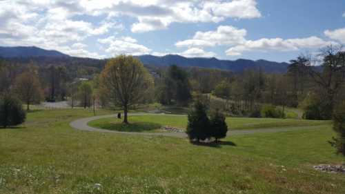 A scenic view of a park with winding paths, trees, and mountains under a partly cloudy sky.