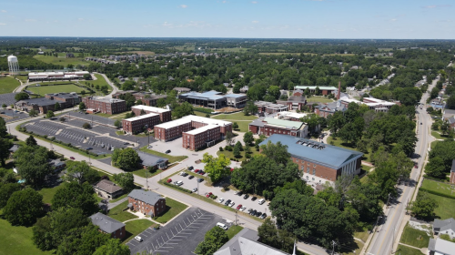 Aerial view of a college campus with multiple buildings, green spaces, and surrounding residential areas.