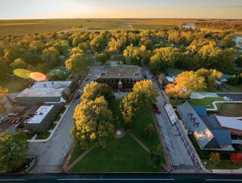 Aerial view of a green park surrounded by trees and buildings, with fields stretching into the distance under a sunset sky.